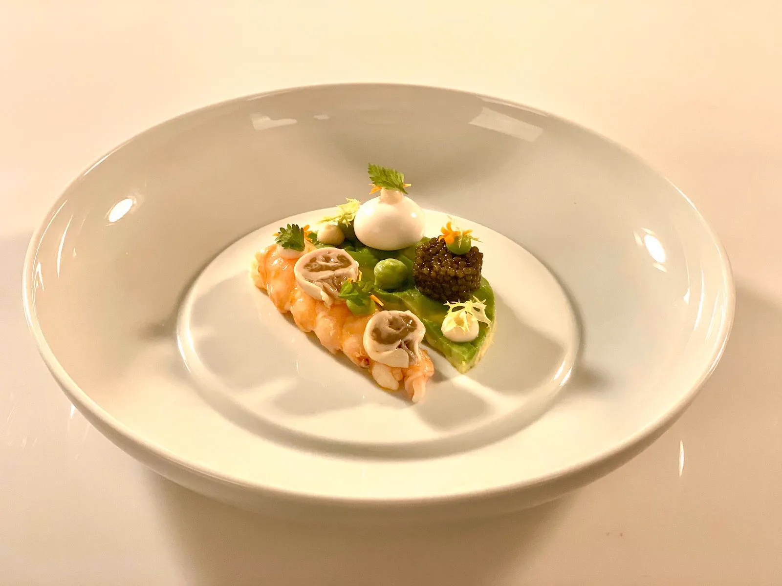 Langoustine tail with imperial caviar, green purée, cream, herbs and edible flowers, plated by a chef in a starred restaurant
